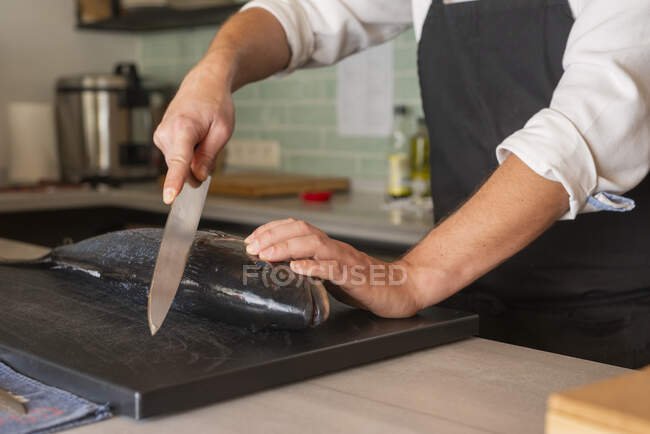 Zugeschnittener, nicht wiederzuerkennender männlicher Koch in Schürze schneidet rohen frischen Fisch am Tisch im Sushi-Restaurant — Stockfoto