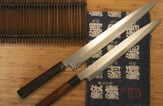 Vue de dessus des couteaux tranchants et du tapis de sushi placés sur la table en bois dans le restaurant asiatique — Photo de stock