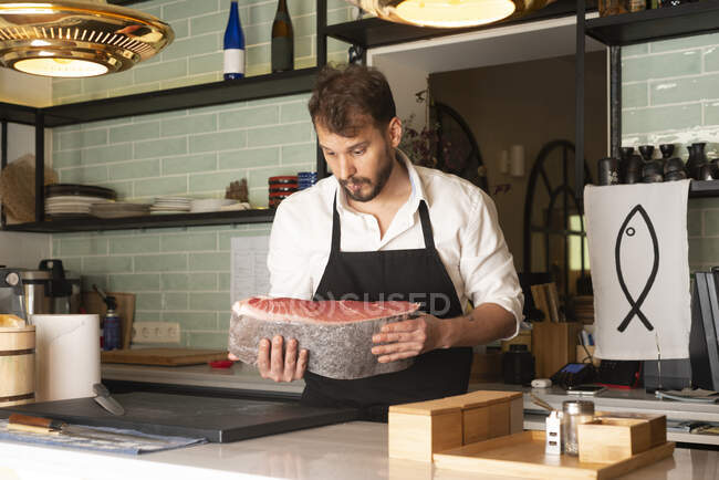 Focused male chef cutting raw fish at table in Asian restaurant and preparing sushi — Stock Photo