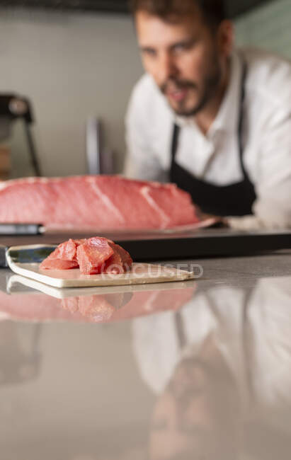 Filet de poisson cru placé sur la planche à découper sur la table dans le restaurant de sushi asiatique sur fond de cuisinier masculin flou — Photo de stock