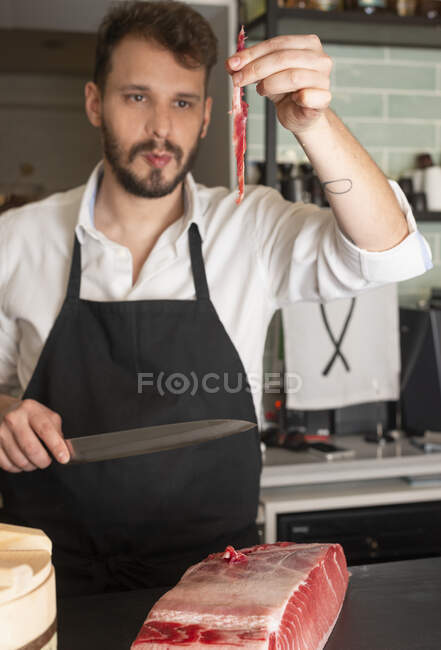 Чоловік готує в фартусі, ріже свіжу рибу, готуючи суші в східному ресторані — стокове фото