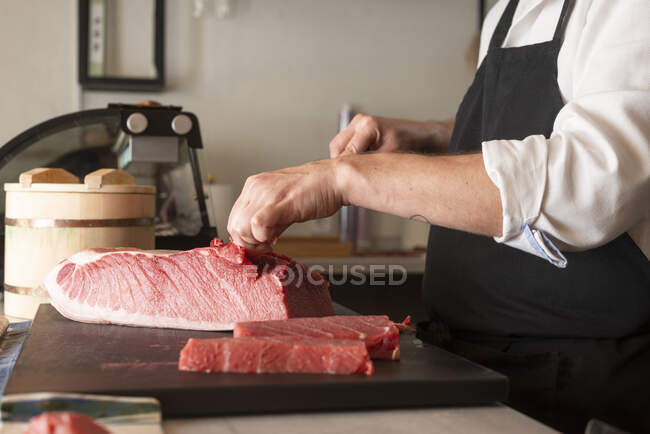 Seitenansicht von zugeschnittenen unkenntlich verwendeten männlichen Koch rohen Fisch am Tisch in einem asiatischen Restaurant schneiden und Sushi zubereiten — Stockfoto