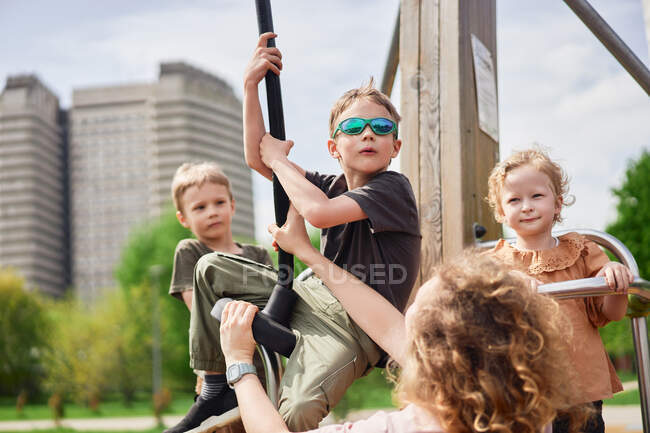 Компания милых детей, играющих вместе на детской площадке в городе, веселясь в солнечный день летом — стоковое фото