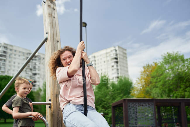 Positive female riding swing rope while laughing and having fun on playground during summer weekend — Stock Photo