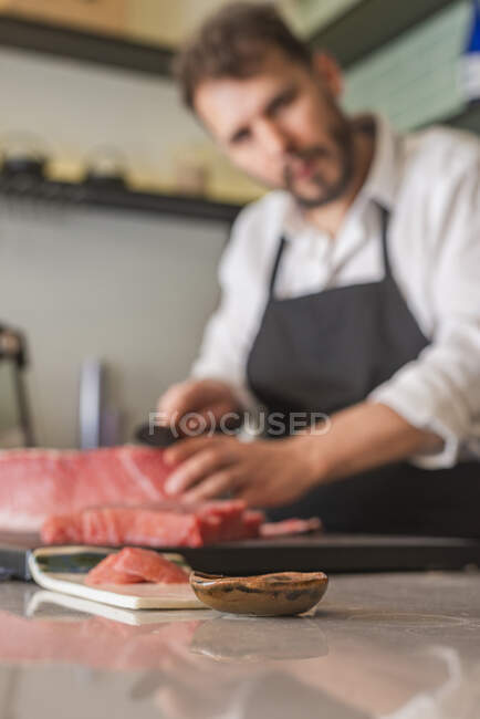 Chef masculino desfocado cortando peixe cru à mesa no restaurante asiático e preparando sushi — Fotografia de Stock