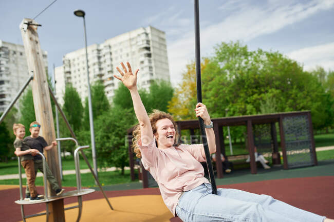 Positive Reiterin reitet Schaukelseil beim Lachen und Spaß auf Spielplatz am Sommerwochenende — Stockfoto