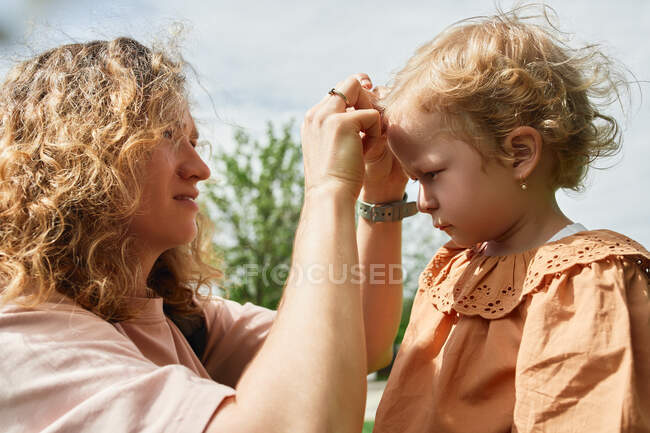 Vista lateral de la madre cariñosa que se preocupa por su hija pequeña mientras pasa tiempo en el parque en el día soleado - foto de stock