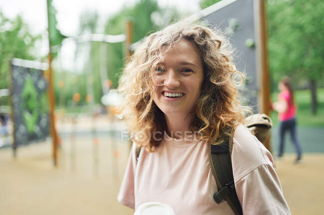 Entzücktes Weibchen mit lockigem Haar steht auf Spielplatz im Park und blickt in Kamera — Stockfoto