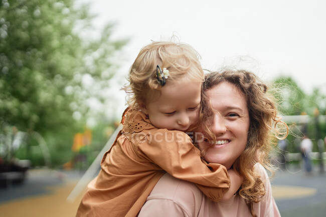 Cute little girl hugging cheerful mother in park while spending weekend together in summer — Stock Photo