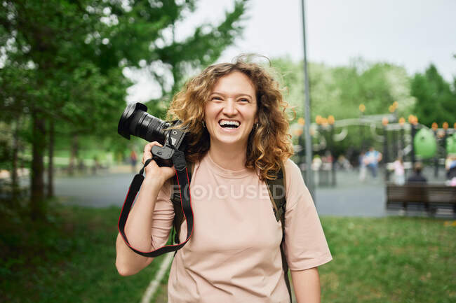 Focused female photographer with modern camera standing in green park and looking away — Stock Photo
