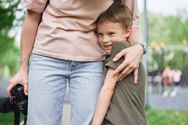 Cortar mãe sem rosto abraçando sorrindo menino bonito enquanto de pé no parque de verão juntos — Fotografia de Stock