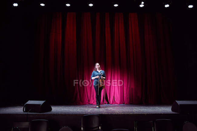 Ganzkörperprofessionelle Geigerin, die während der Probe live auf der Bühne im leeren Konzertsaal auftritt und in die Kamera blickt — Stockfoto