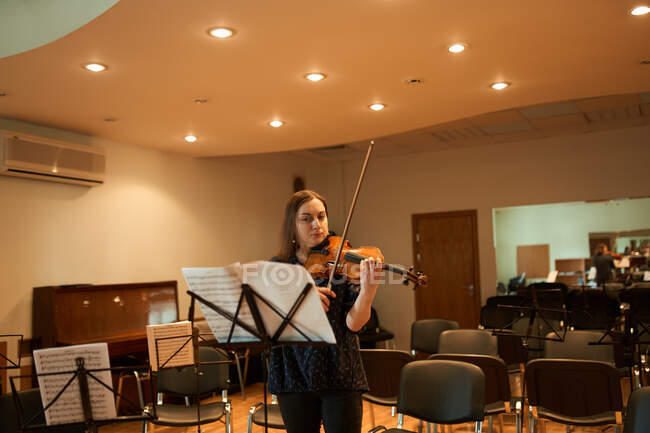 Música profesional tocando el violín acústico y mirando la hoja de música durante el ensayo en el estudio - foto de stock