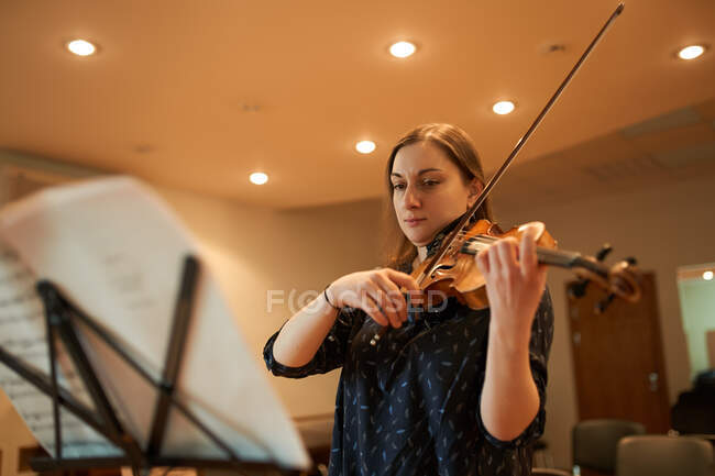 Професійна жінка-музикантка грає на акустичній скрипці і дивиться на музичний аркуш під час репетиції в студії — стокове фото