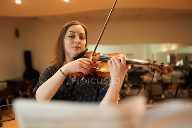 Músico profissional focado tocando violino acústico e olhando para a folha de música durante o ensaio em estúdio — Fotografia de Stock
