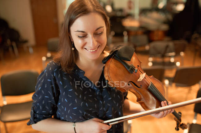 Fröhliche Profimusikerin spielt akustische Geige und betrachtet Notenblätter während der Probe im Studio — Stockfoto