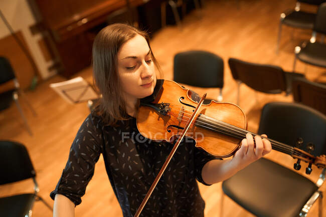 From above focused professional female musician playing acoustic violin with eyes closed with music sheet during rehearsal in studio — Stock Photo