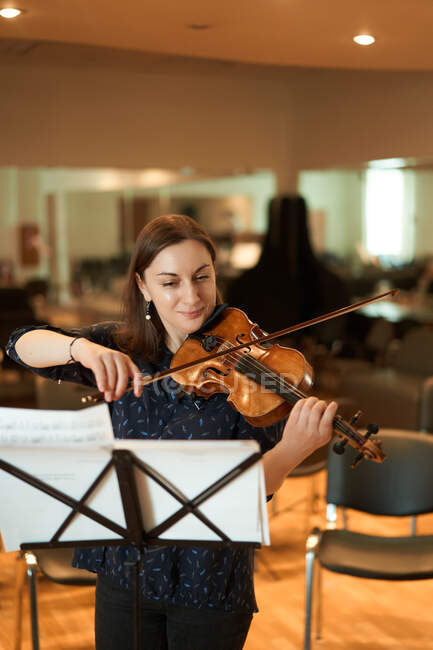 Профессиональная женщина-музыкант играет на акустической скрипке и смотрит на ноты во время репетиции в студии — стоковое фото