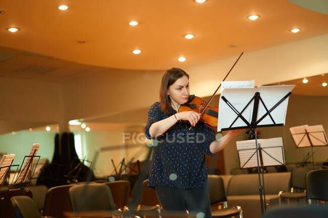 Зосереджена професійна жінка-музикантка грає на акустичній скрипці і дивиться на музичний аркуш під час репетиції в студії — стокове фото