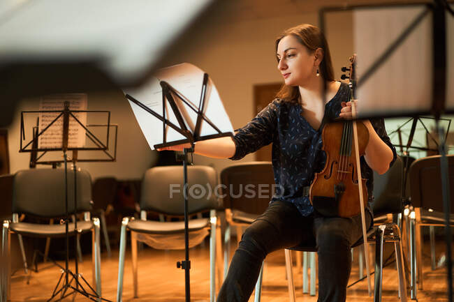 Focused professional female musician playing acoustic violin and looking at music sheet during rehearsal in studio — Stock Photo