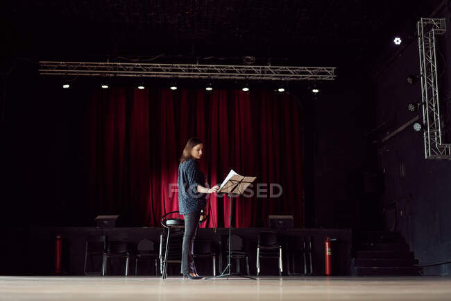 Visão lateral músico feminino focado com violino leitura de partituras na sala de concertos perto do palco — Fotografia de Stock