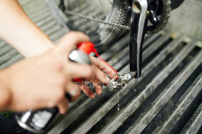 From above of crop anonymous male master using chemical spray and cleaning bike pedal in repair workshop — Stock Photo