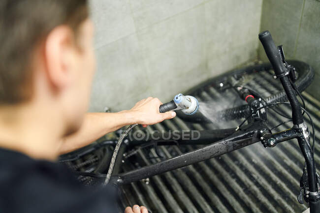High angle of faceless male master washing modern bike with water in repair workshop — Stock Photo