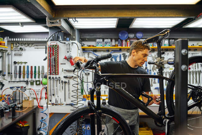 Сфокусований чоловік-технік прикріпляє колесо до велосипеда, працюючи в професійній сучасній майстерні. — стокове фото