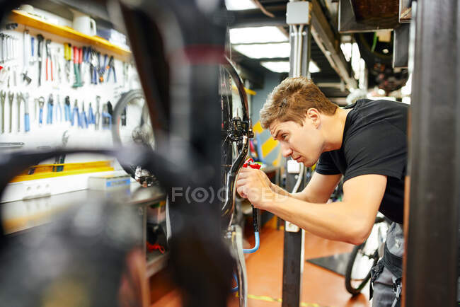 Vue latérale du pneu de pompage mâle concentré de la roue de vélo à l'aide d'un pistolet de gonflage en atelier — Photo de stock