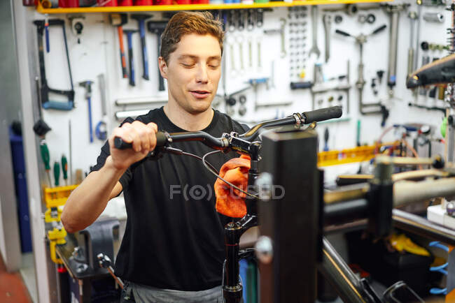 Focado macho mestre limpando quadro de bicicleta com pano enquanto trabalhava na oficina de reparação moderna — Fotografia de Stock