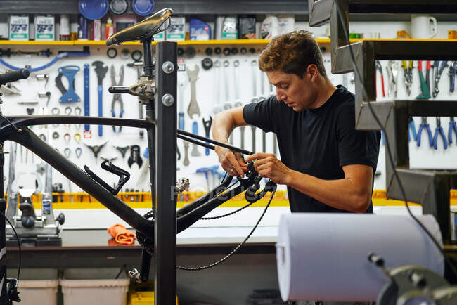 Marco masculino enfocado de la bici del limpiamiento principal con el trapo mientras que trabaja en taller moderno de la reparación - foto de stock