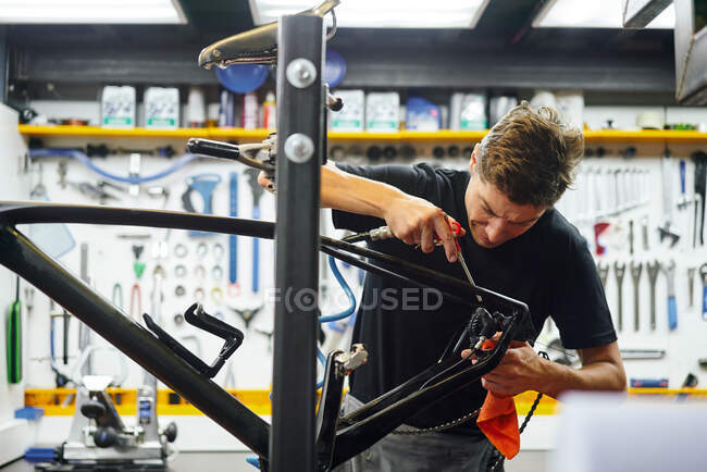 Focado macho mestre limpando quadro de bicicleta com pano enquanto trabalhava na oficina de reparação moderna — Fotografia de Stock