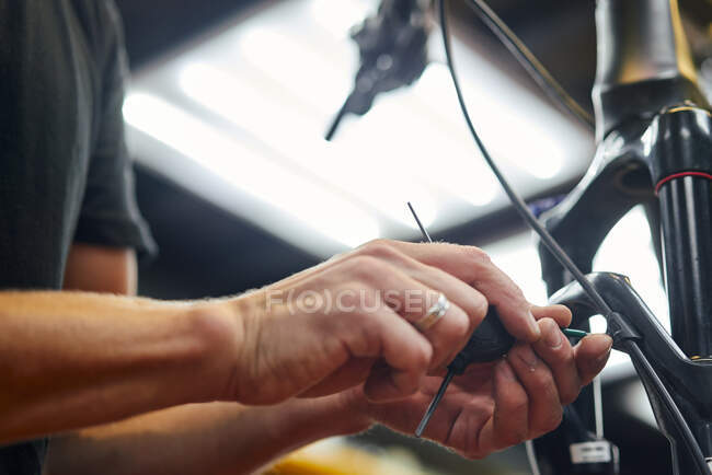 Crop anonymous male mechanic repairing brake cable of bike in workshop — Stock Photo