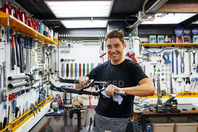 Зосереджений майстер витирає раму велосипеда ганчіркою під час роботи в сучасних ремонтних майстернях, дивлячись на камеру. — стокове фото