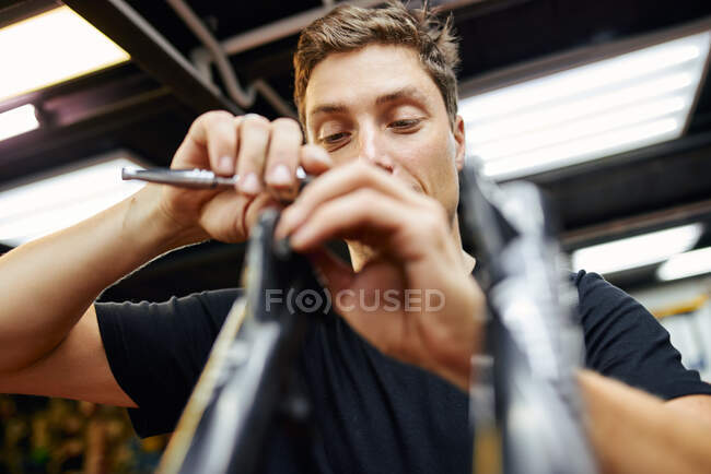 Baixo ângulo de homem aparafusar em parte da bicicleta enquanto trabalhava na oficina de reparo profissional — Fotografia de Stock