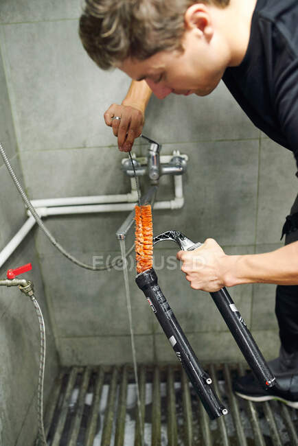 Vista lateral do mestre masculino focado limpeza garfo de bicicleta de metal com escova na oficina — Fotografia de Stock