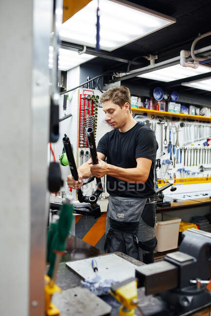 Maestro masculino enfocado con marco de bicicleta trabajando en taller de reparación moderno - foto de stock