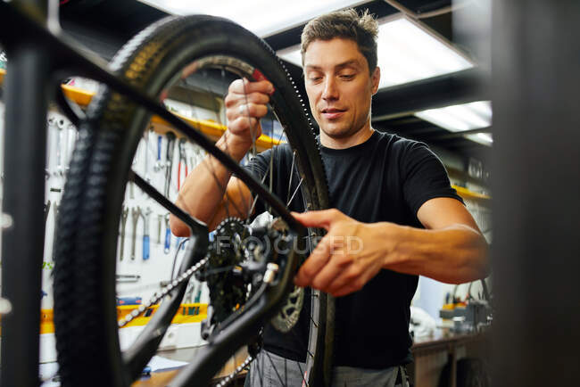 Technicien masculin attachant la roue au vélo tout en travaillant dans un atelier moderne professionnel — Photo de stock