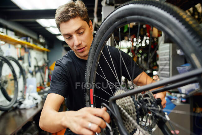 Чоловічий технік прикріплює колесо до велосипеда під час роботи в професійній сучасній майстерні — стокове фото