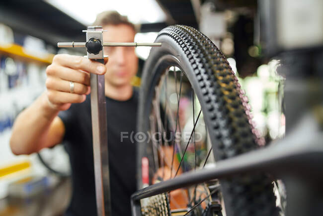 Blurred male master centering bicycle wheel placed on truing stand in modern repair workshop — Stock Photo