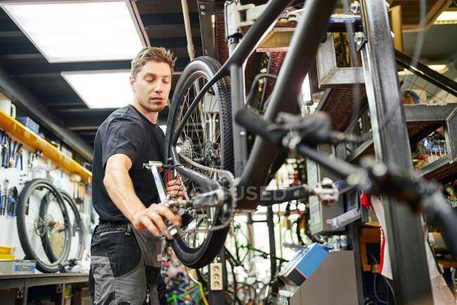 De baixo do mecânico masculino focado usando a chave de encaixe e reparando a roda de bicicleta na oficina — Fotografia de Stock