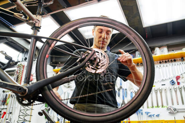 Técnico masculino que fija la rueda a la bici mientras que trabaja en taller moderno profesional - foto de stock