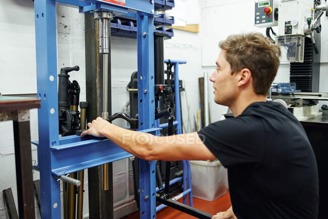 Vista lateral do homem adulto usando prensa hidráulica enquanto trabalhava na oficina de reparo moderna — Fotografia de Stock