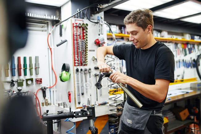 Cheerful male master fixing metal bicycle fork while working in contemporary repair workshop — Stock Photo