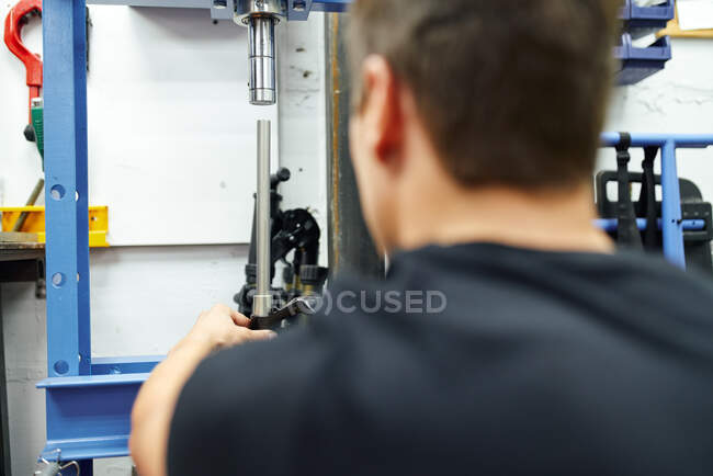 Обратный вид взрослого мужчины с помощью гидравлического пресса во время работы в современной ремонтной мастерской — стоковое фото