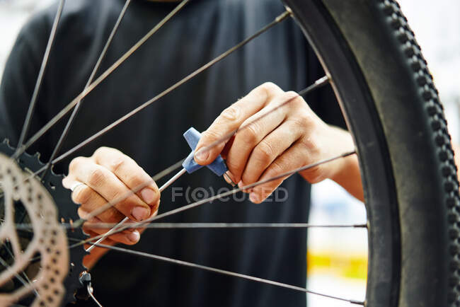 Unrecognizable man in black t shirt screwing in wheel while fixing bicycle in garage — Stock Photo