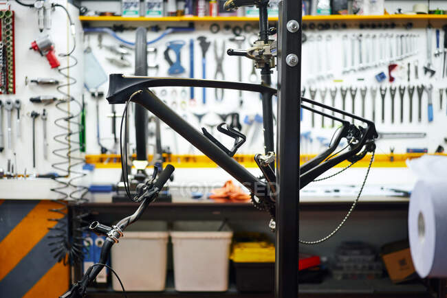 Рамка современного велосипеда, висящего на стойке против верстака и стены с инструментами в ремонтной мастерской — стоковое фото