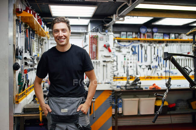 Glücklicher männlicher Mechaniker lächelt und blickt mit Werkzeug in Garage gegen Wand — Stockfoto