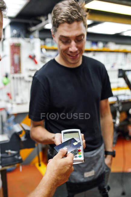 Crop customer putting credit card over contactless terminal to pay to mechanic for repair service in modern garage — Stock Photo