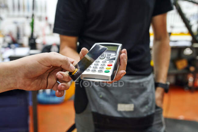 Low angle of crop client using smartphone to pay to male technician in repair workshop — Stock Photo